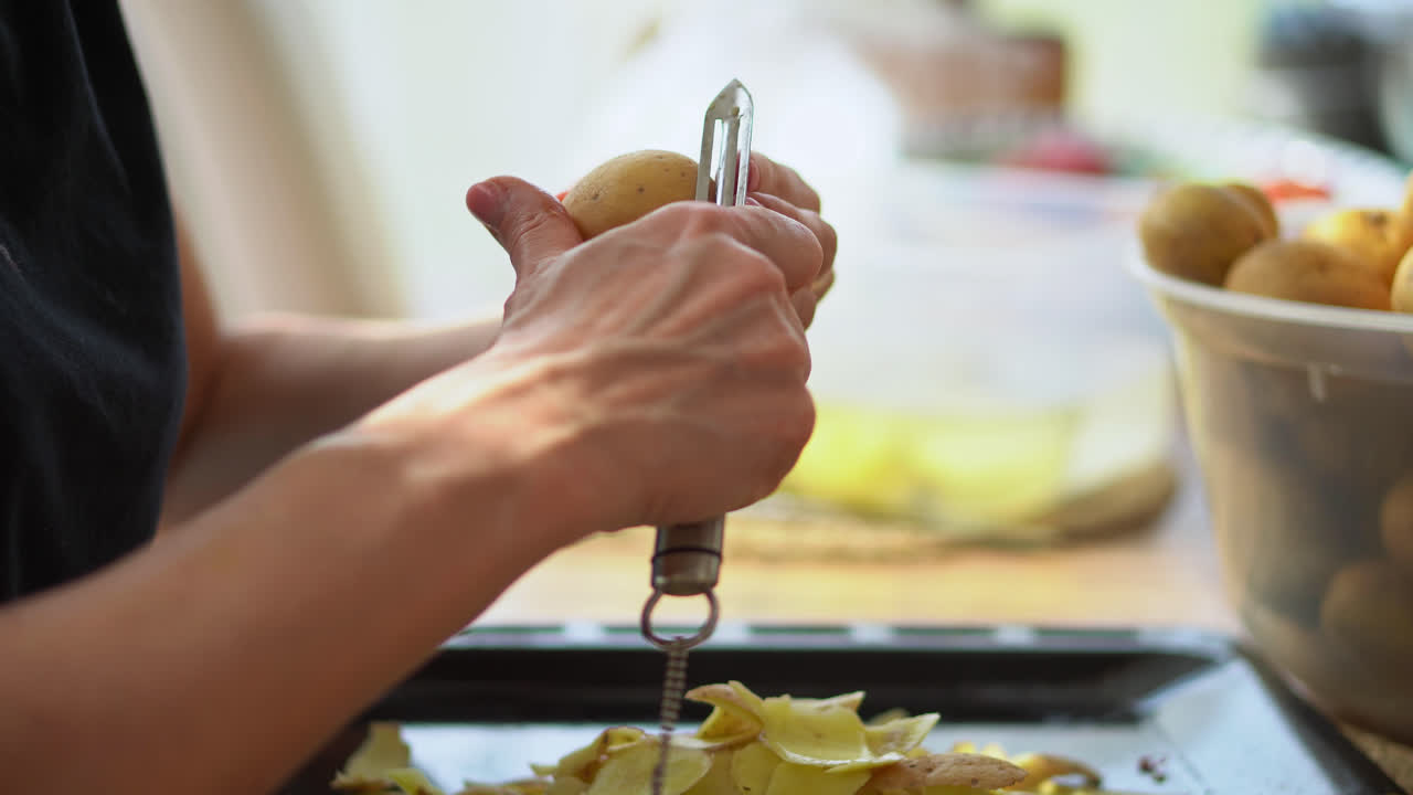 mano recortada de una mujer sosteniendo un pelador pelando muchas papas en la cocina