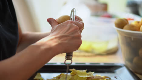 Mano-Recortada-De-Una-Mujer-Sosteniendo-Un-Pelador-Pelando-Muchas-Papas-En-La-Cocina