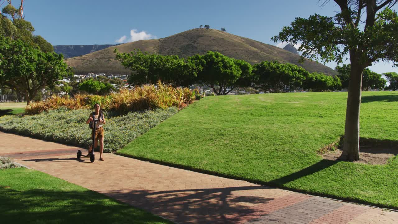 mujer afroamericana con mochila montando un scooter en el parque