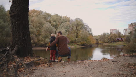 travelling in forest or park at autumn day man is talking with his little son father and child are enjoying nature viewing lake in forest
