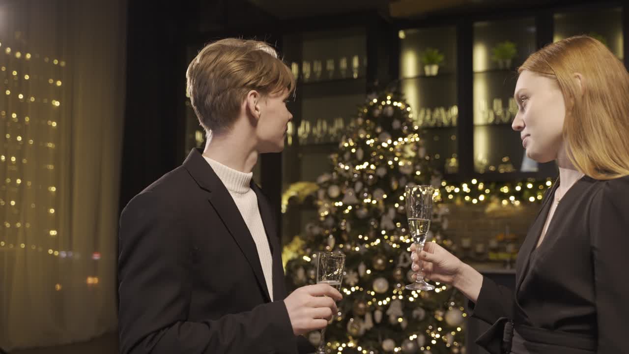 A woman and a man dressed in elegant clothes toast with a glass of champagne and take a sip at the new year's party