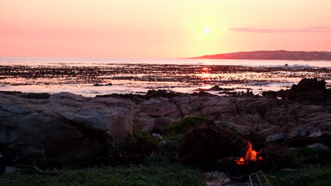 relaxing fire burns in portable barbecue during vivid sunset on overstrand coast