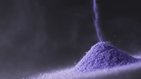 Video-of-close-up-of-purple-sand-grains-pouring-into-heap-and-copy-space-on-black-background