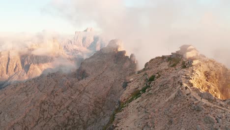 Person-hike-trail-up-to-Rifugio-Nuvolau-wrapped-with-thin-clouds,-sunset-aerial