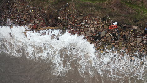 la cámara aérea se desplaza a lo largo de una playa llena de basura mientras las olas golpean la orilla