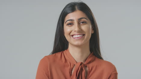 Head-And-Shoulders-Studio-Portrait-Of-Smiling-Young-Businesswoman-Against-Plain-Background