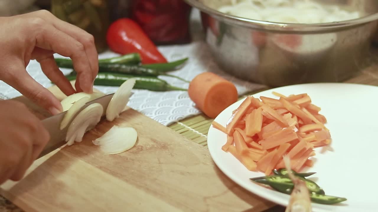 Slicing white onions and setting it aside on a plate, candid kitchen scene of ingredients preparation for home cooking a meal