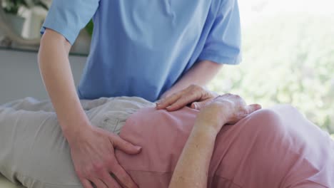 female health worker massaging hips of senior woman at home