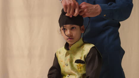 fotografía de estudio de un padre atando un turbante a la cabeza de un joven sikh que lleva un chaleco tradicional como secuencia parte 6 de 10