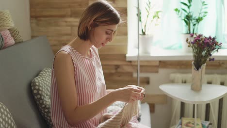 Craft-woman-knitting-wool-sitting-on-couch-in-room-on-background-window