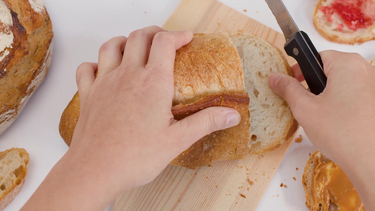 Person Slicing Fresh Loaf of Sourdough Bread on Wooden Board