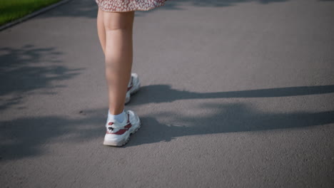 close-up of woman s legs walking on tarred road, with shadow casting along the path, wearing white and red sneakers, this urban scene captures motion, light, and casual style