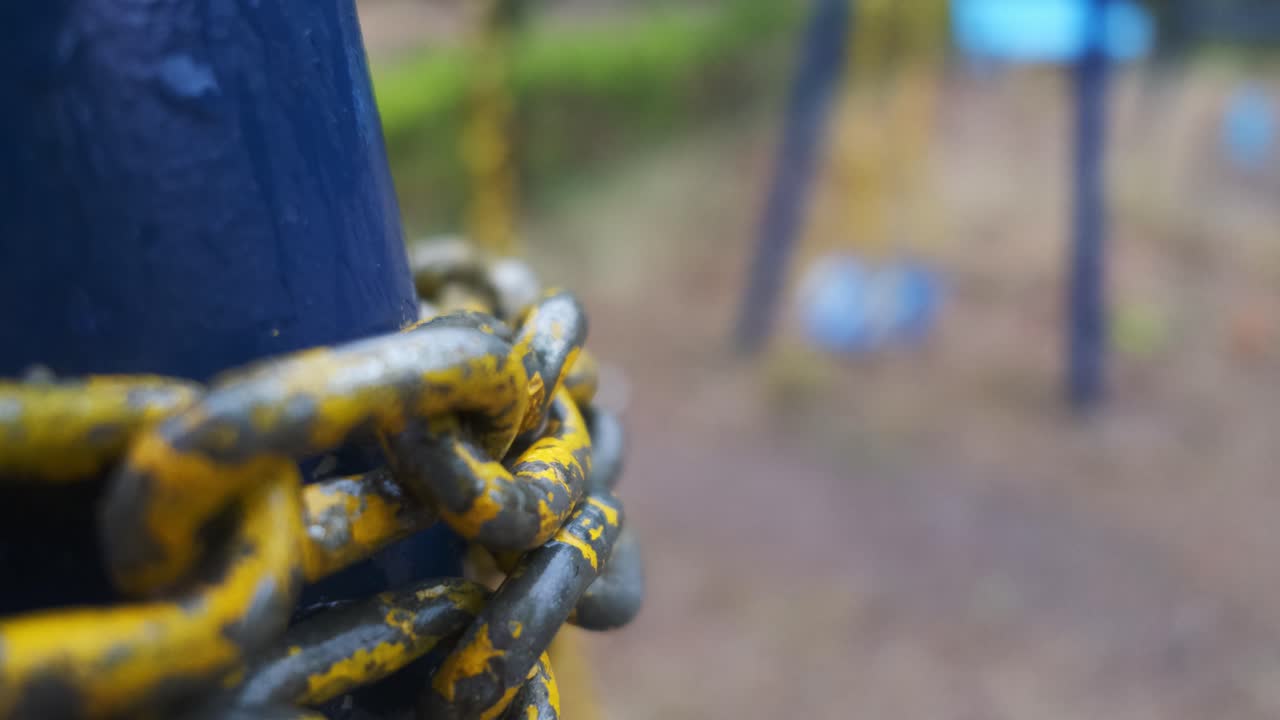 Chipped yellow chain links in the foreground with a swaying swing in the background