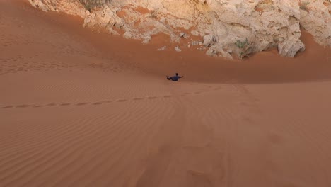 male tourist sand boarding down desert dune in dubai