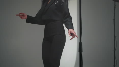 faceless woman in a black suit dancing slowly in a softly blurred studio setting