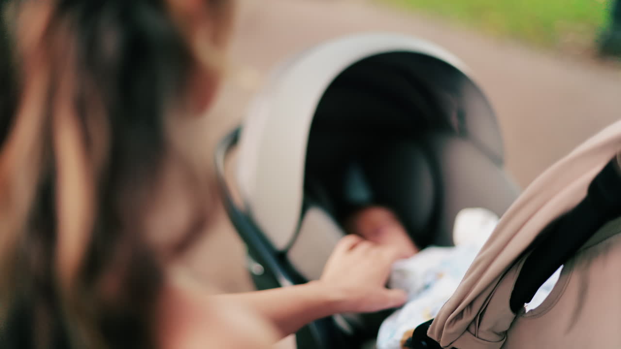 A woman with long curly hair holding a stroller while sitting on a park bench surrounded by greenery
