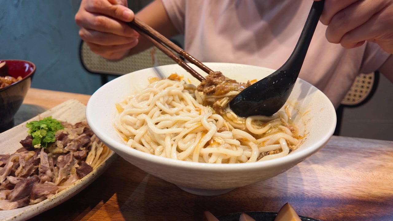 Cận cảnh đôi tay dùng đũa và thìa để trộn mì cay ở Bangkok, Thái Lan