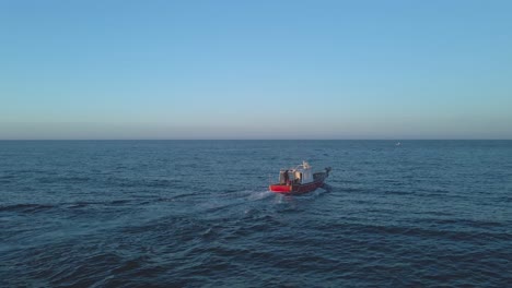 Pequeño-Barco-Pesquero-En-Aguas-Abiertas-Cerca-De-Playa-Del-Cura,-España-Por-La-Noche-Contra-Un-Cielo-Azul-Claro--ángulo-Bajo-Aéreo