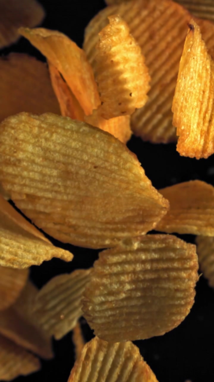 Golden Ridged Potato Chips Falling in Slow Motion on Black Background
