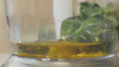 anonymous cook adding olive oil to basil leaves before blending