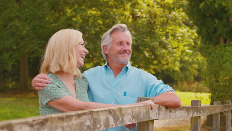 smiling casually dressed mature or senior couple leaning on fence on walk in countryside