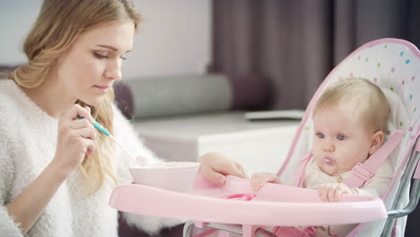 hermosa mujer alimentando al bebé en la silla. mamá alimentando al niño con comida en puré