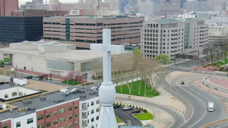 Vista-Aérea-Alrededor-De-Una-Cruz-De-Iglesia,-Con-Fondo-De-Calle-De-La-Ciudad---Dando-Vueltas,-Disparo-De-Drones