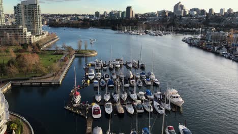 Multiple-pleasure-yachts-moored-at-scaffoldings-at-each-sides-of-the-false-creek-inlet-in-downtown-Vancouver-between-high-buildings-on-a-cloudy-day