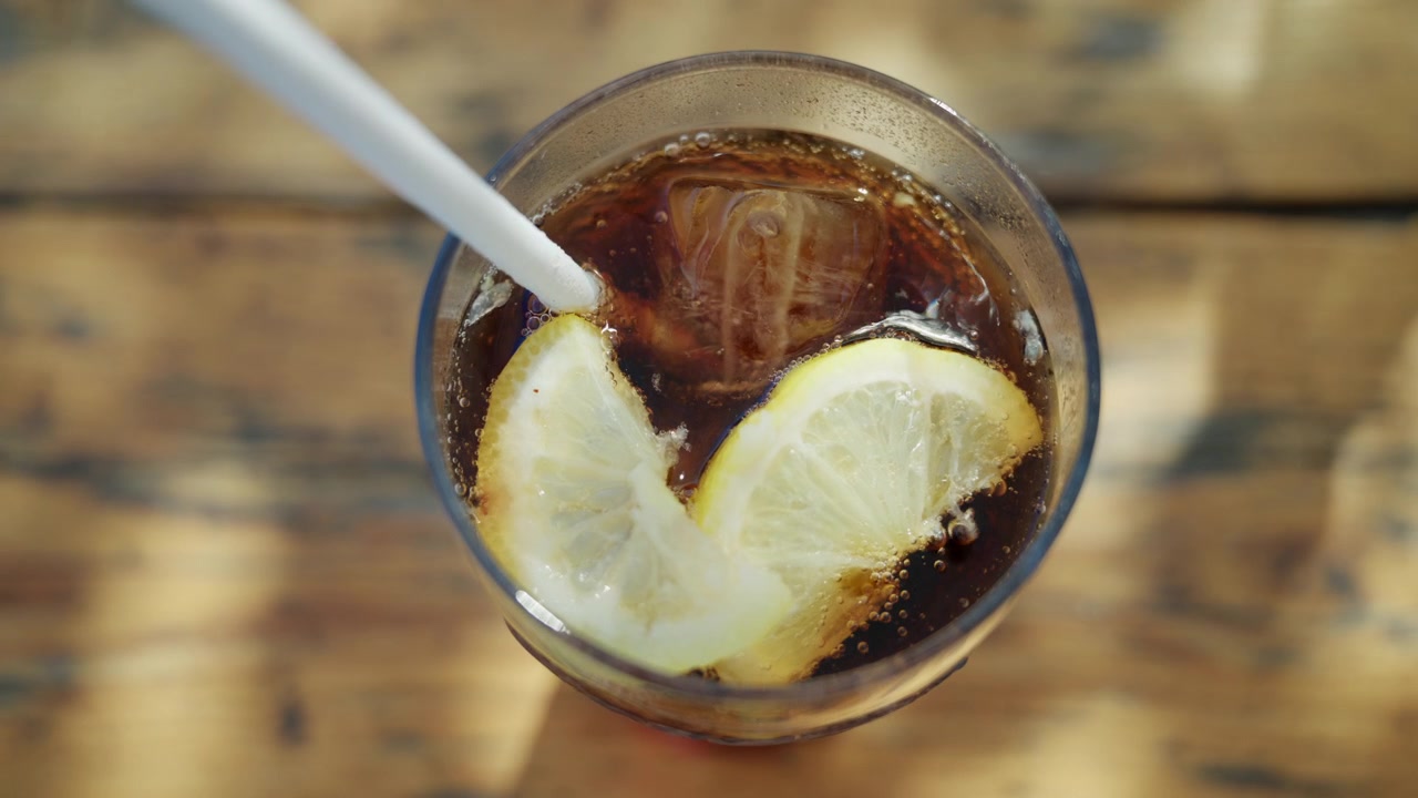 Primo piano di una cola ghiacciata con fette di limone e bollicine in un bicchiere trasparente.