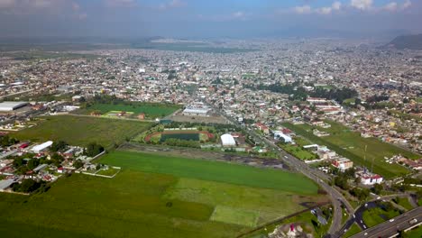 Top-drone-view-of-a-soccer-field-in-the-charming-town-of-chalco-Mexico,-and-view-of-the-highway-town-and-houses-population-density