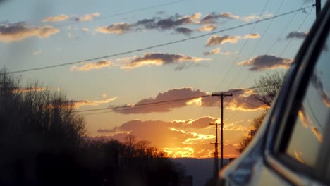 una impresionante puesta de sol dorada que se refleja en el espejo del coche mientras conduce por una carretera rural