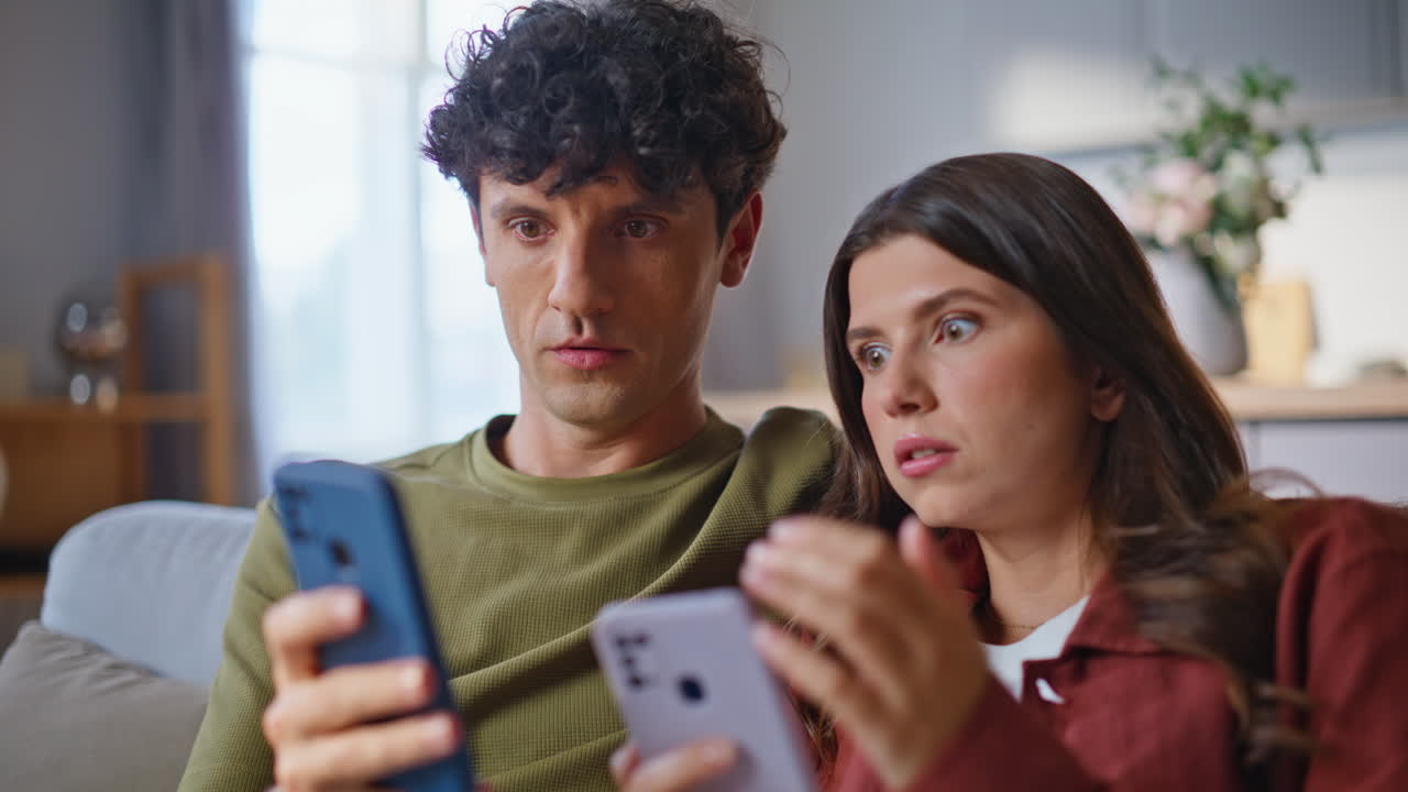 Shocked lovers reacting smartphones news at room closeup. Surprised sweethearts