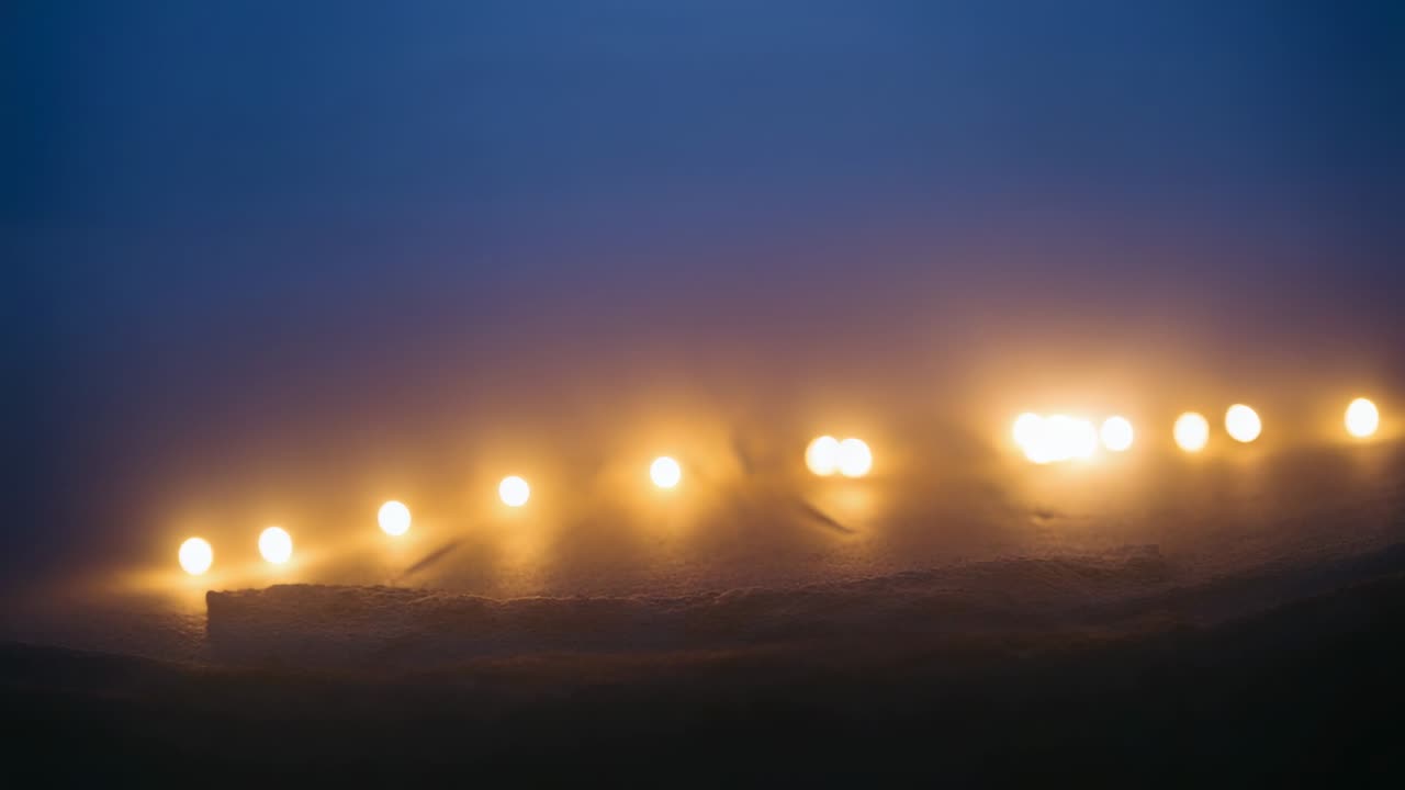 Pulling focus, camera bringing warm lights on horizon into sharper view at dusk with mist halos