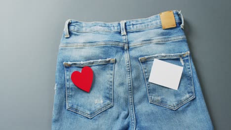 Close-up-of-jeans-with-heart-and-white-note-on-grey-background-with-copy-space