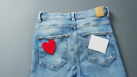 close up of jeans with heart and white note on grey background with copy space