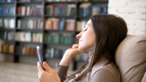 happy peaceful woman relaxing on cozy sofa listening to calm classical music with wireless headphones enjoying lazy weekend hobby alone at home. close up side view of woman on background of home library