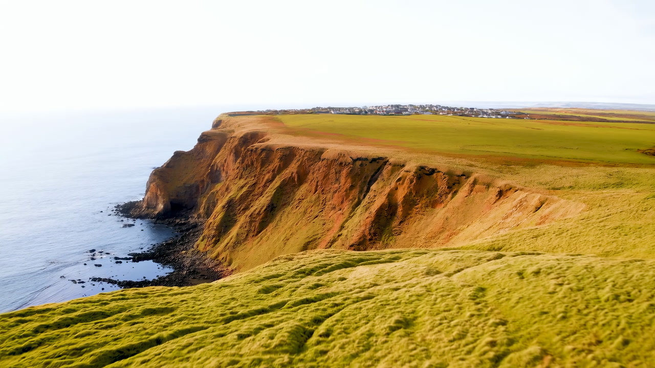 Golden Cliff Coastline Overlooking Calm Sea With Sunlit Grassy Headland, Rugged Eroded Cliffs, Gentle Waves