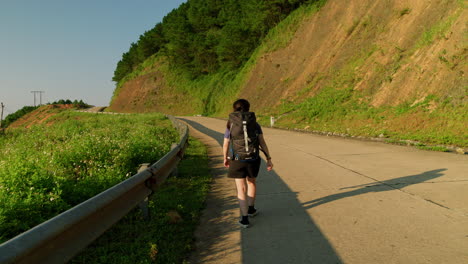 young woman begins her journey as she steadily walks up a hill while wearing a backpack for adventure