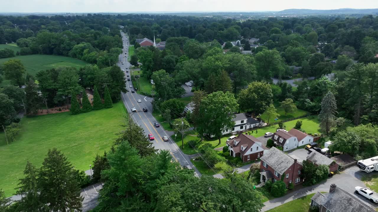 Scena di traffico intenso su strada rurale tra case e abitazioni di periferia. Giorno d'estate. Con alberi verdi in Pennsylvania, America. Zona residenziale con erba verde in giardino. Inquinamento ambientale da fumi