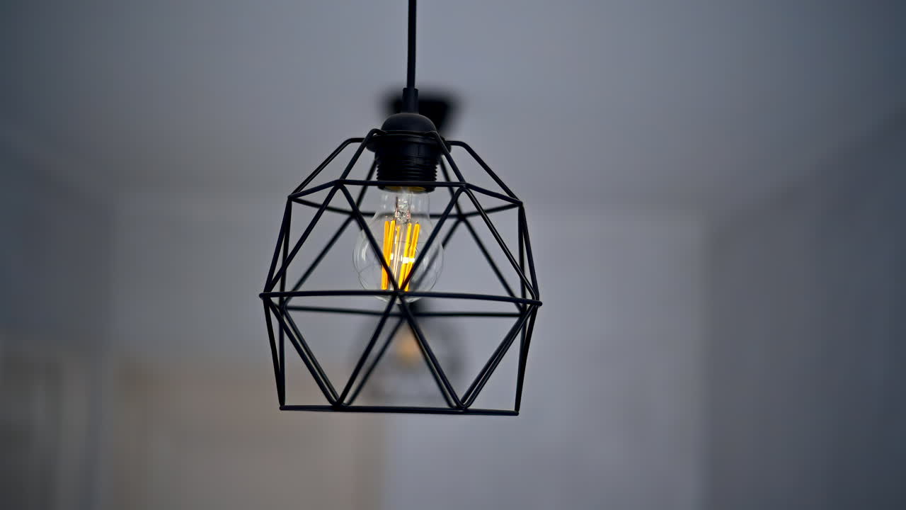 A stylish black metal light fixture is suspended from the ceiling, casting a warm glow in a contemporary indoor setting. The geometric design enhances the room's ambiance