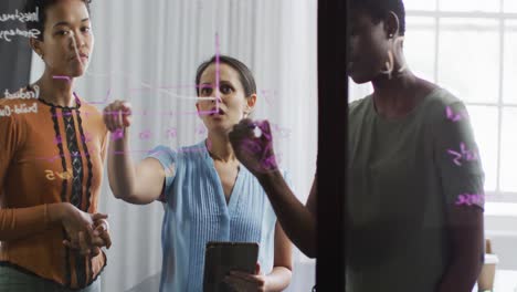 Diverse-businesswomen-standing-at-glassboard,-brainstorming-in-office