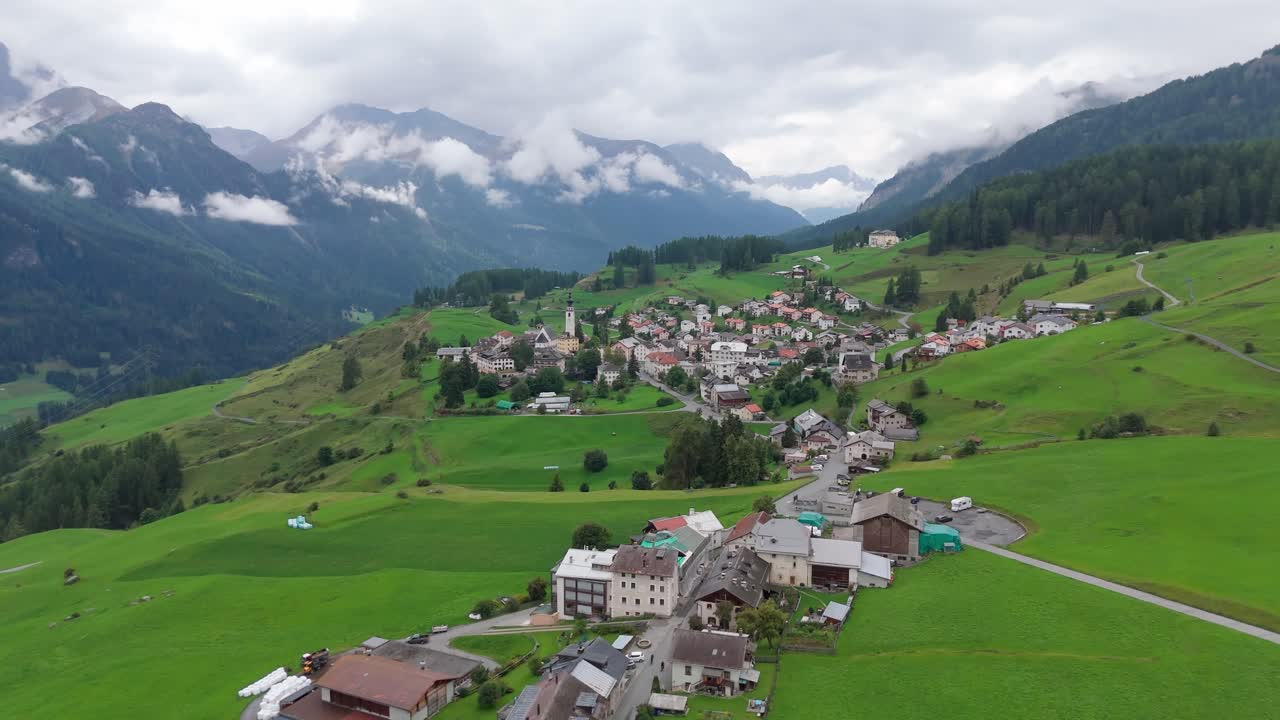 Drone flyover peaceful and idyllic village in Switzerland. Cloudy summer day between alp mountains. Panorama view. Apartments and huts in town