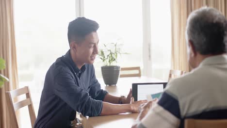 Diverse-financial-advisor-and-senior-man-discussing-paperwork-and-using-tablet-at-home,-slow-motion