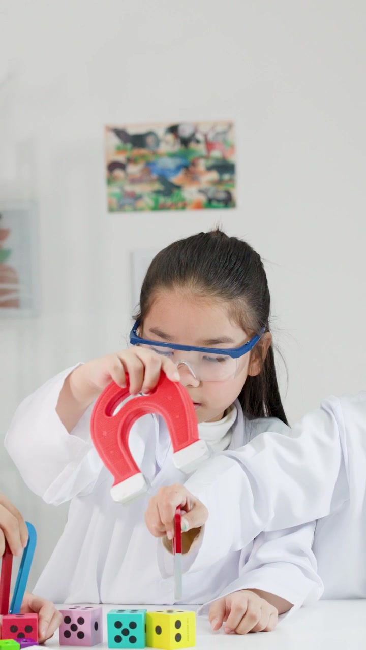 Anak-anak Asia mengenakan kacamata pengaman dan jas lab menjelajahi sifat magnetik menggunakan magnet tapal kuda di ruang kelas.