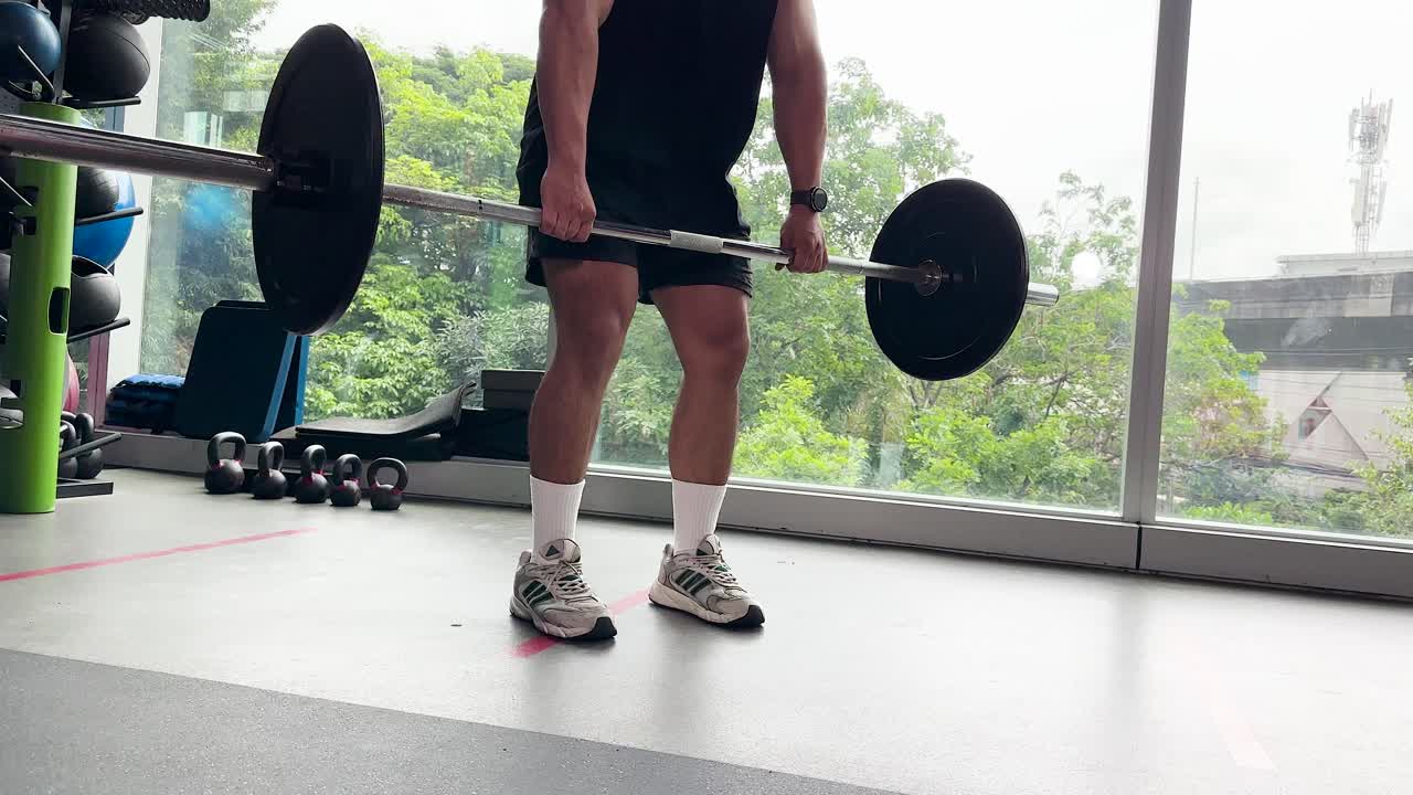Athletic man executes barbell deadlift in bright gym with large windows and natural daylight
