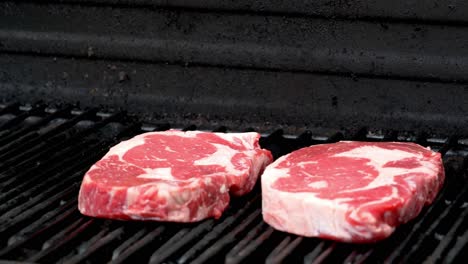 two raw rib-eye steaks getting ready to cook on a grill