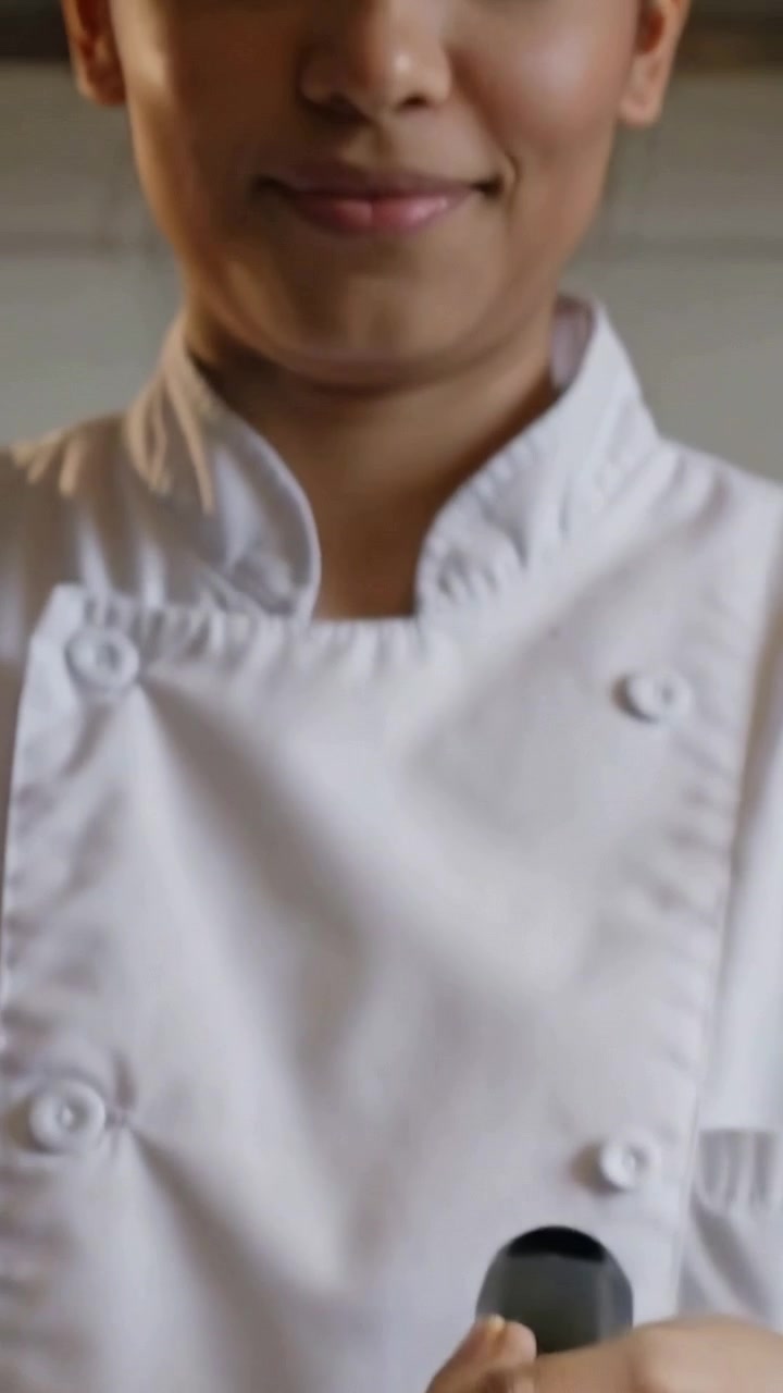 Video verticale: Primo piano di uno chef che cucina in cucina, stabilizzando il manico della padella, con dettagli di rivetti, un cucchiaio e il camice bianco
