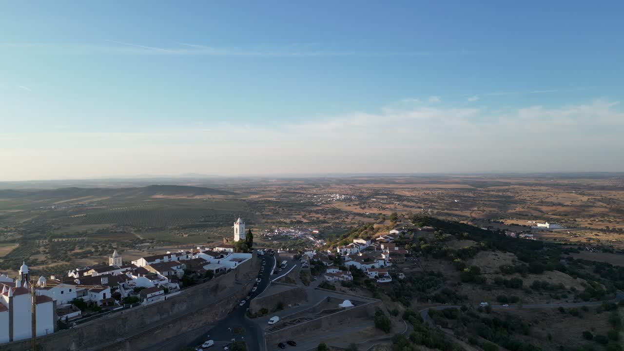 Rotating aerial view of Monsaraz, a historic hilltop village in Portugal. Featuring whitewashed houses, medieval walls, and panoramic views of the Alentejo plains under a serene blue sky.