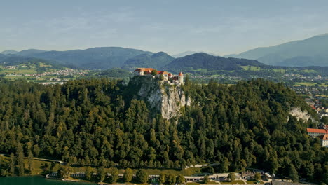 slovenia bled castle appears in forested hillside, aerial orbit