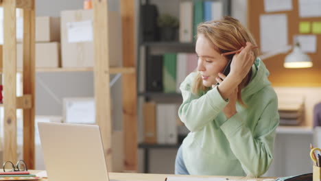 mujer hablando por teléfono y trabajando en una computadora portátil en la oficina